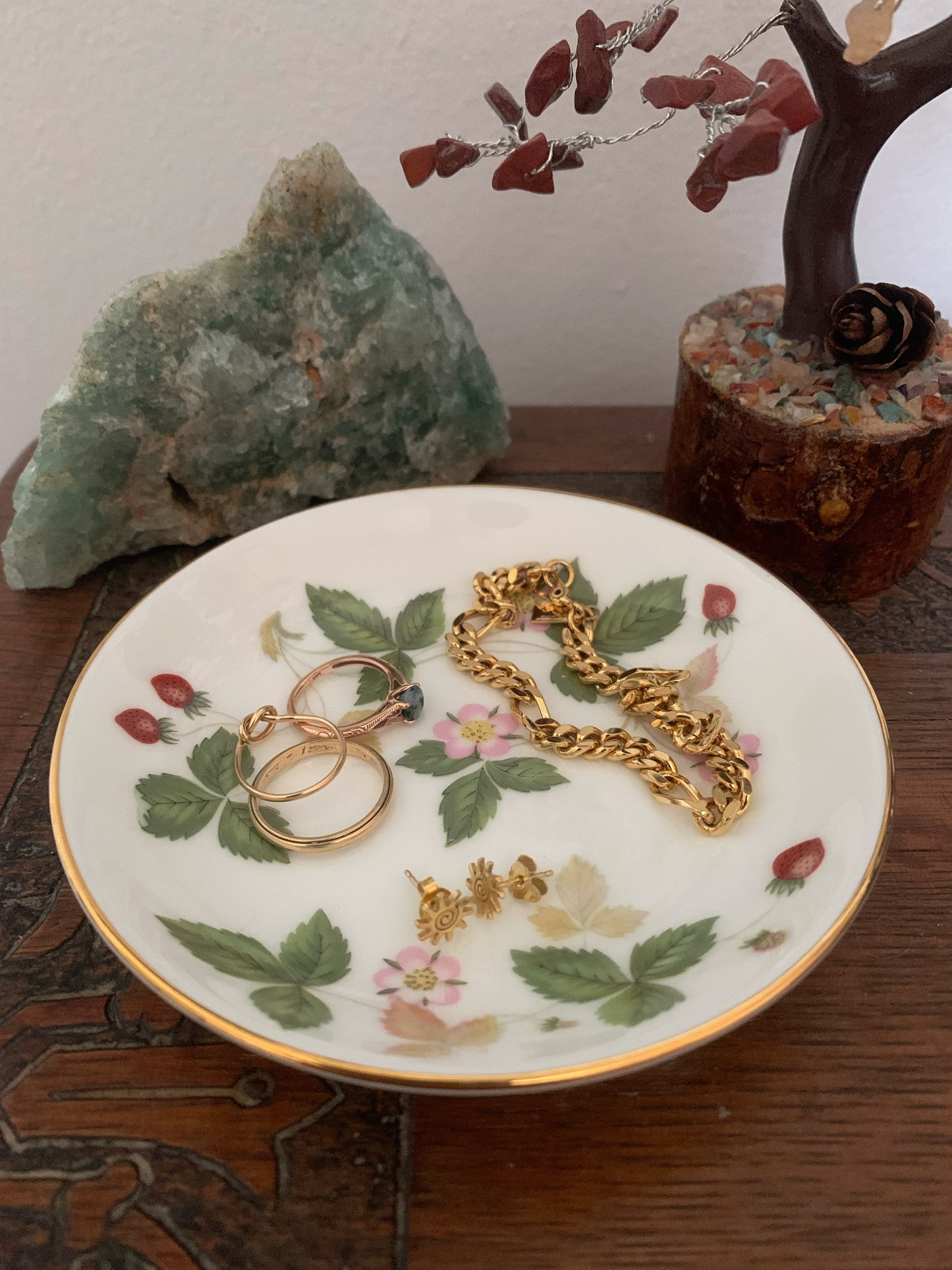 Decorative plate with floral design holding gold jewelry on a wooden surface.