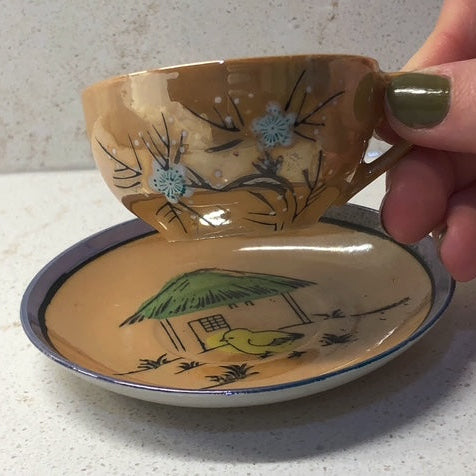 Ceramic teacup and saucer with artistic designs held by a hand.