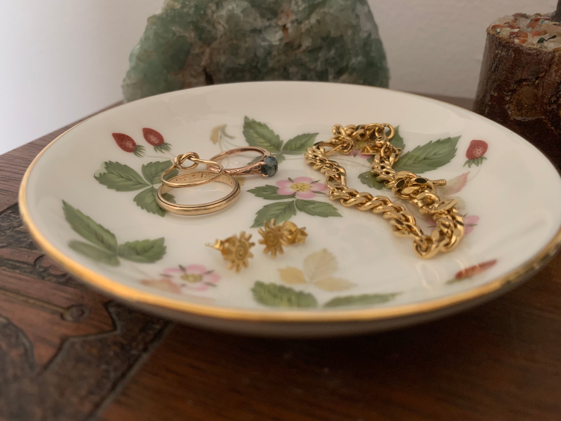 Jewelry including rings and a gold chain on a decorative plate with floral patterns.