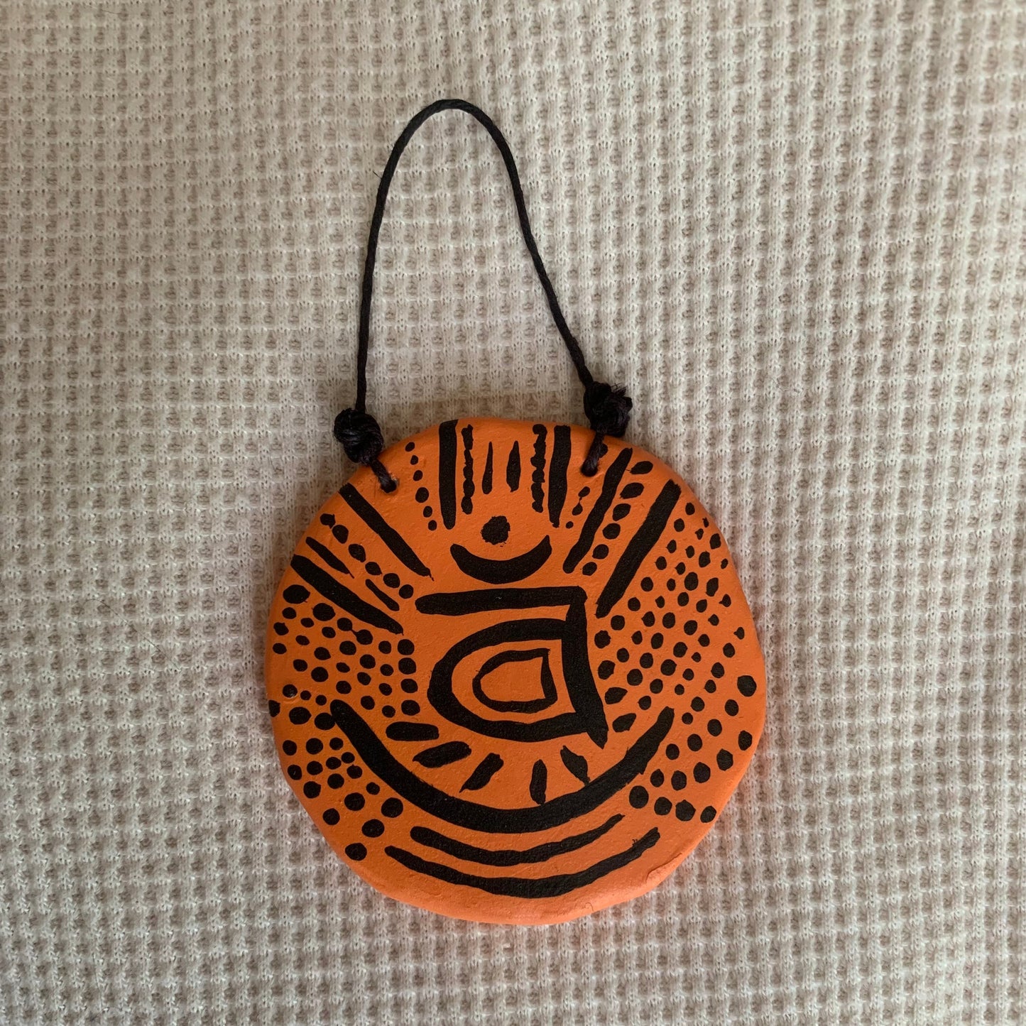 Round orange pendant with black design on a textured beige background